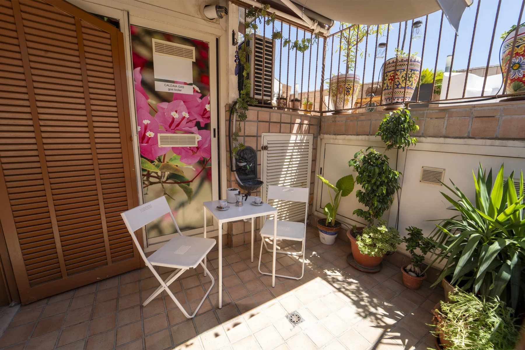 A small tiled patio with a table, seating, and potted plants.