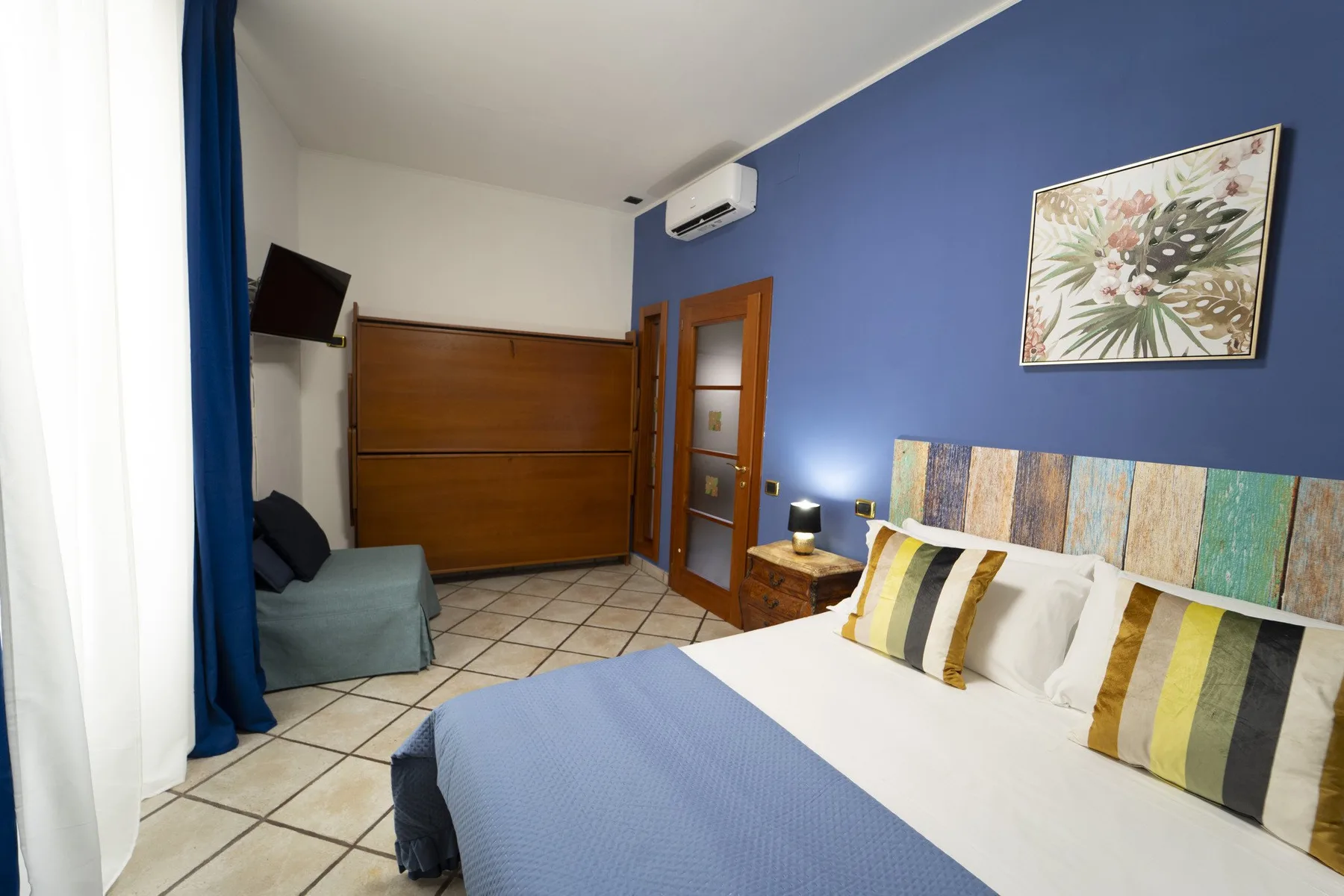 A bedroom with a bed, striped pillows, and a blue accent wall.