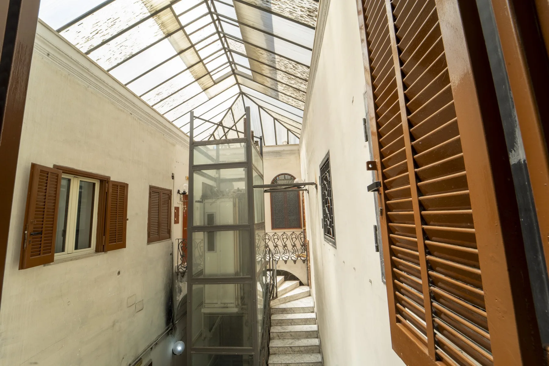 A narrow indoor courtyard with a glass-roofed stairwell and shuttered windows.
