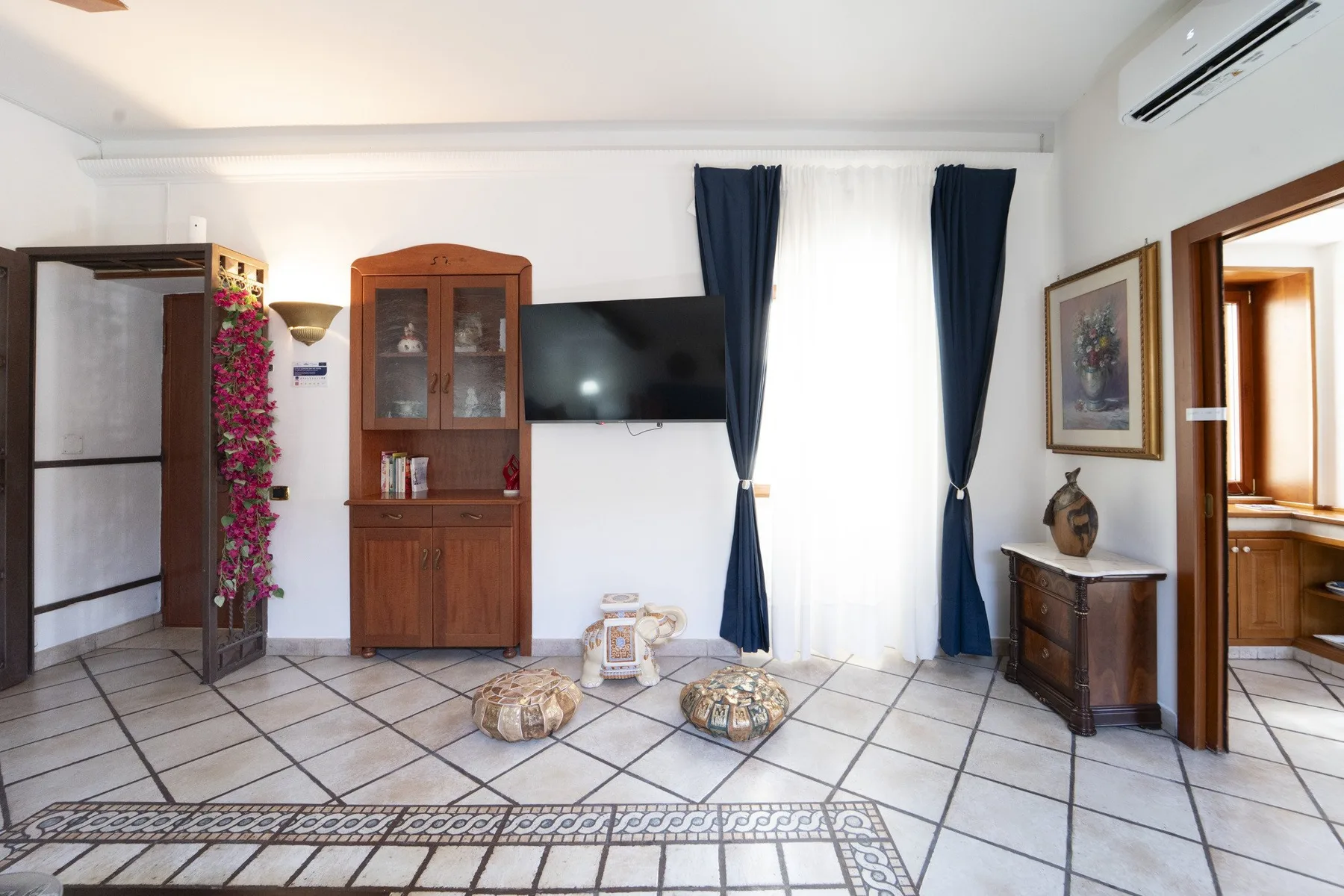 A bright living room with a television, wooden cabinets, and dark curtains.