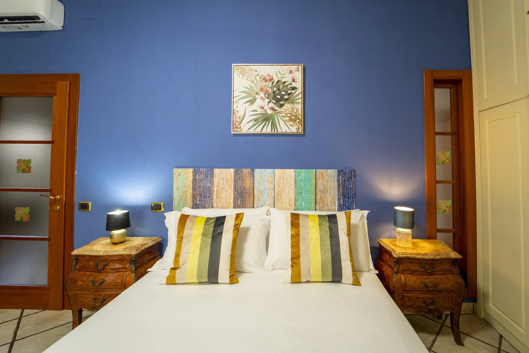 A bedroom with a bed, striped pillows, and a colorful headboard.