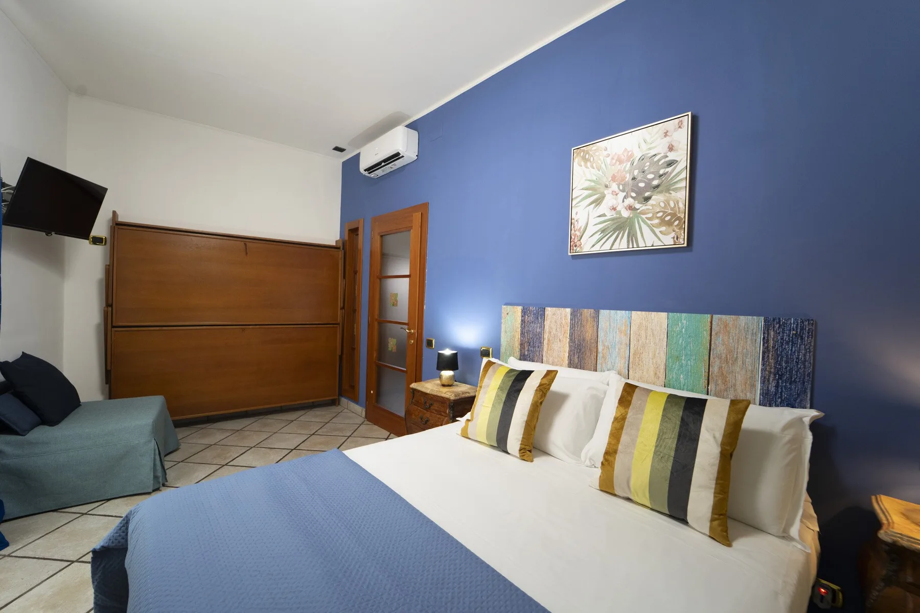A bedroom with a white bed, colorful striped pillows, and a blue accent wall.
