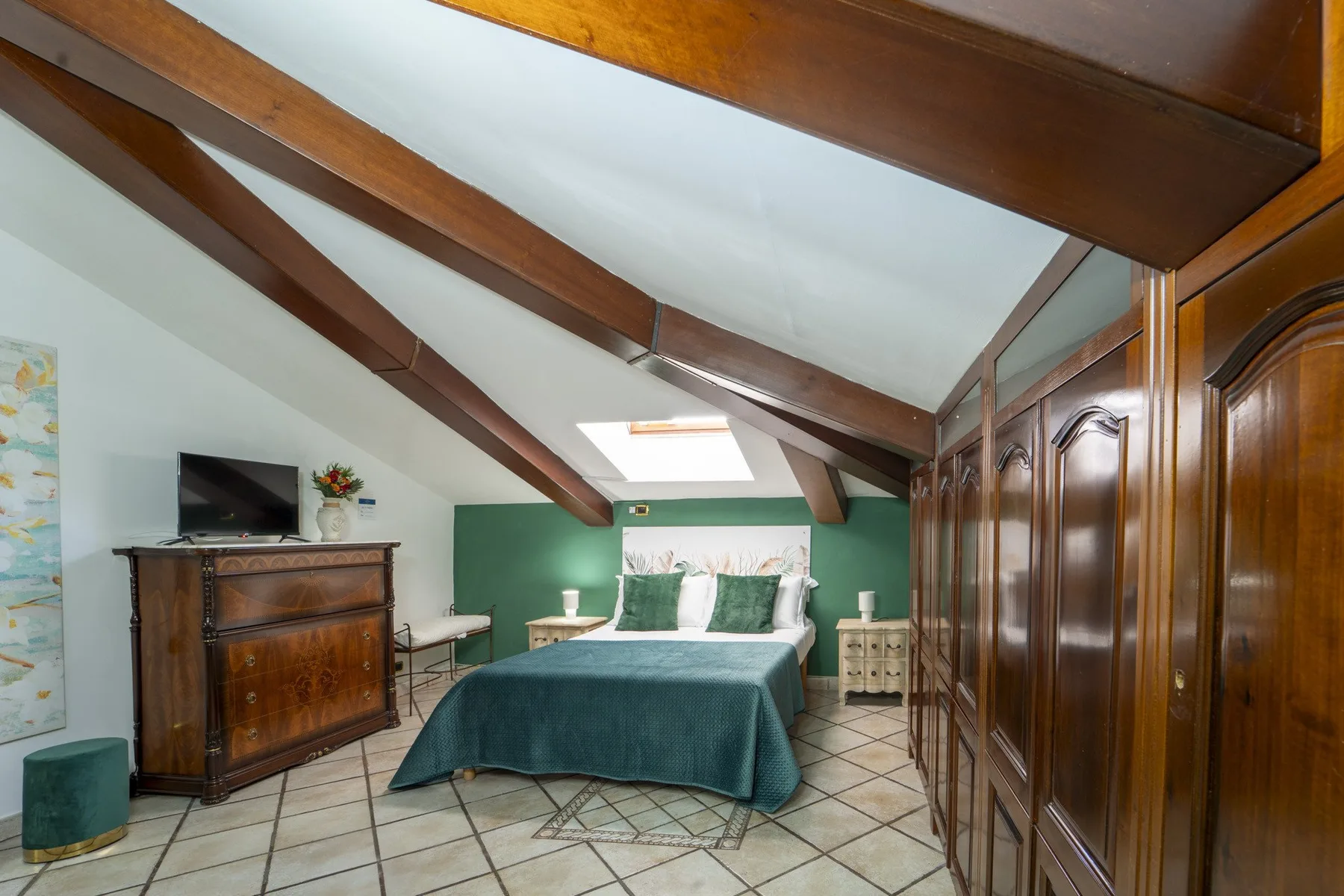 A bedroom with a bed, dark wooden wardrobes, and sloped ceiling beams.