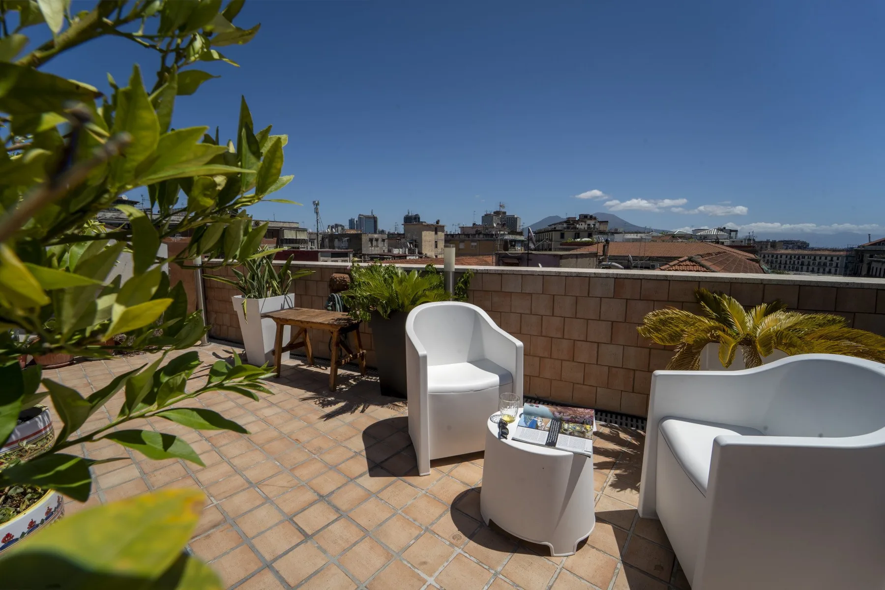 A rooftop terrace with outdoor seating and potted plants under a clear blue sky.
