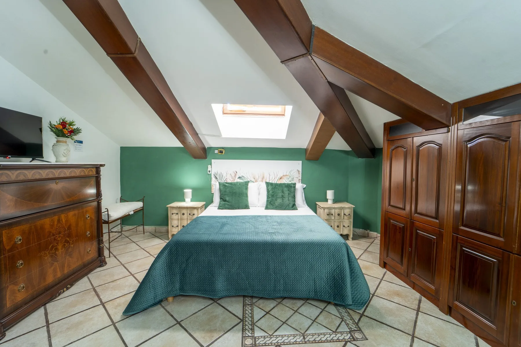 A bedroom with a bed beneath sloped ceilings and exposed wooden beams.