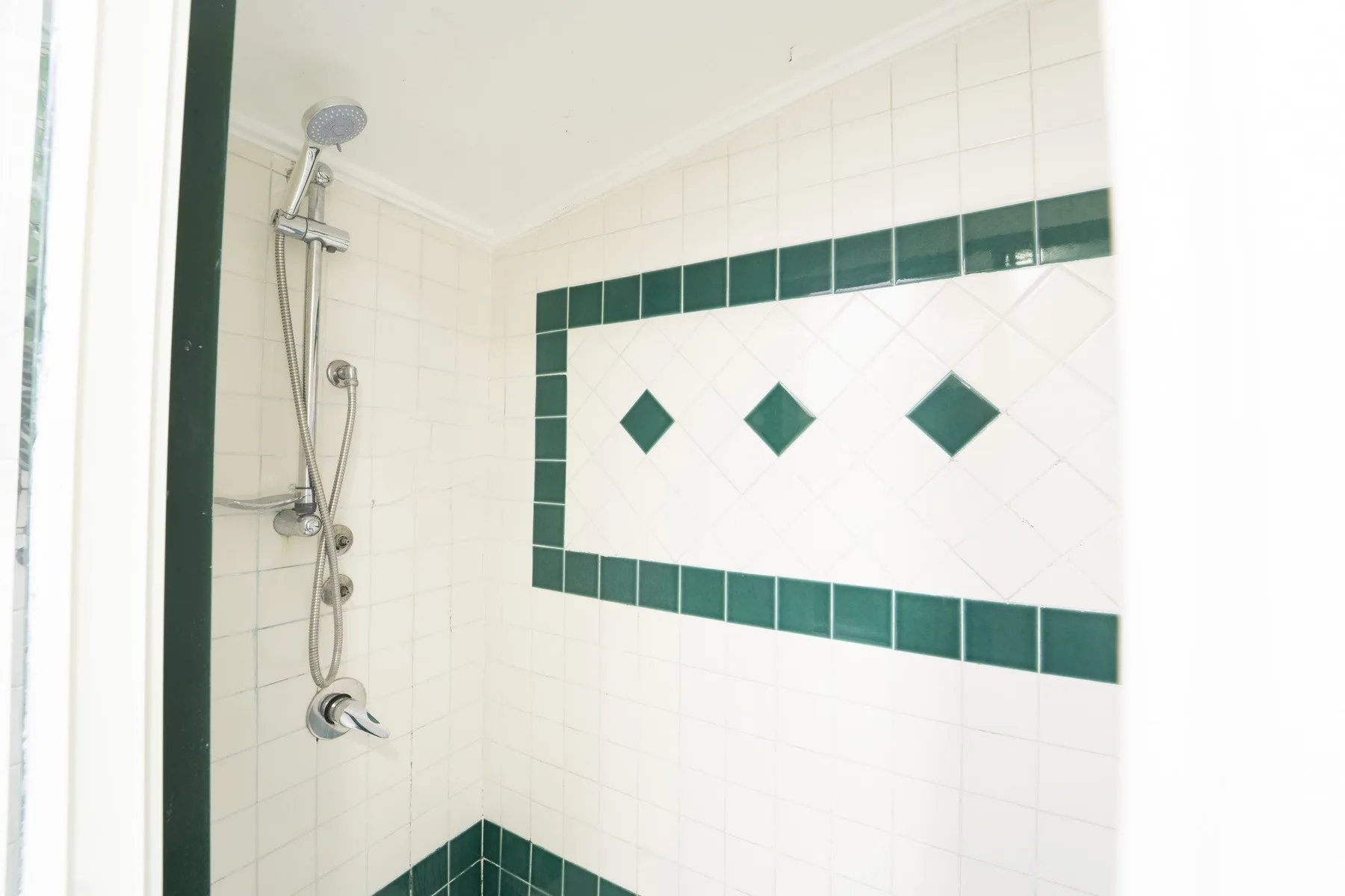 A tiled shower area with dark green accents and a wall-mounted showerhead.