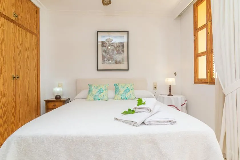 A bright bedroom with a neatly made bed and framed artwork above it.