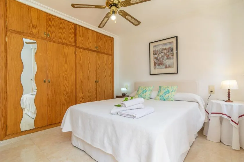 A bedroom with a white bed beside a large wooden wardrobe.