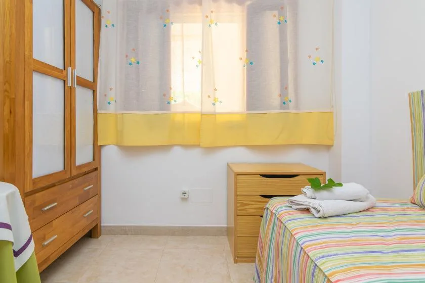 A bedroom with a colorful striped bedspread and a wooden wardrobe.