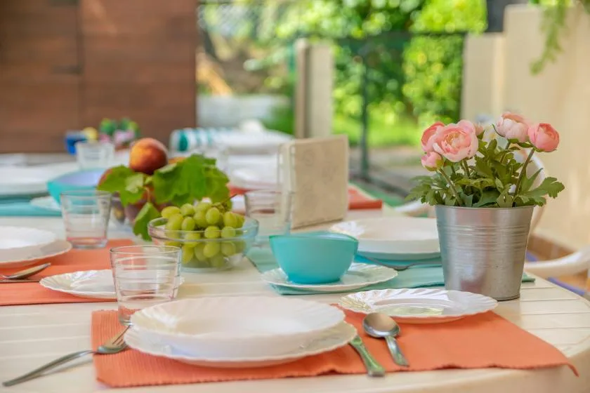 A dining table is set with plates, colorful napkins, fruit, and flowers.
