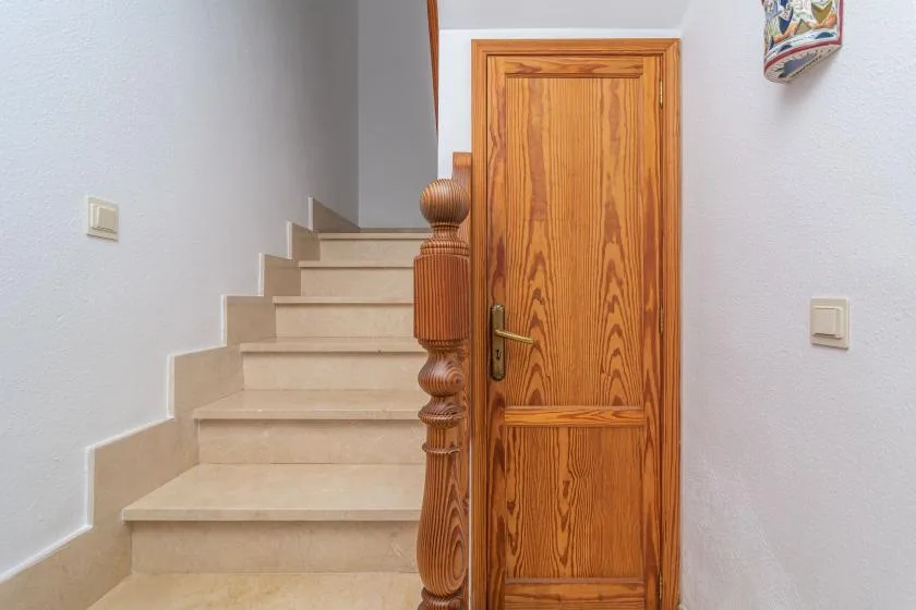 A staircase rises beside a wooden door in a bright interior hallway.