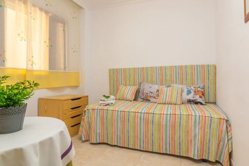 A bedroom with a colorful striped bed and a potted plant beside a small table.