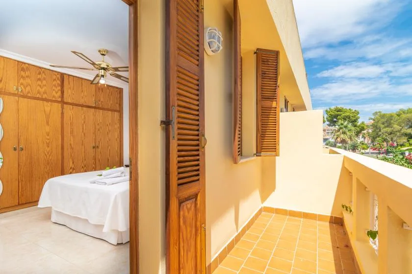 A sunlit balcony with terracotta tiles overlooks a bedroom with a bed.