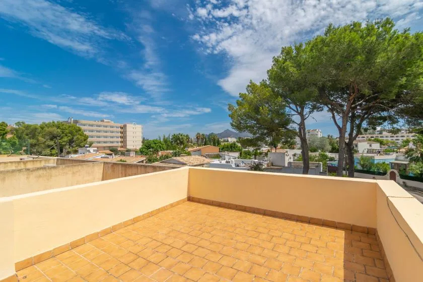 A sunny tiled terrace overlooks trees and nearby buildings.