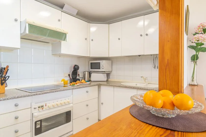 A bright kitchen with white cabinets, a countertop, and a bowl of oranges.