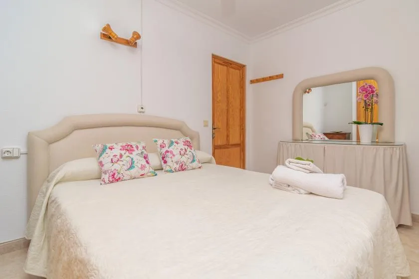 A bedroom with a large bed, floral pillows, and a mirror on the wall.