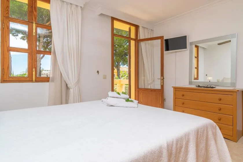 A bedroom with a neatly made bed, wooden windows, and a dresser.