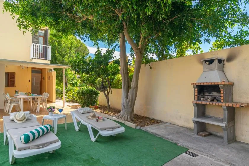 An outdoor patio with lounge seating, a large shade tree, and a built-in barbecue.