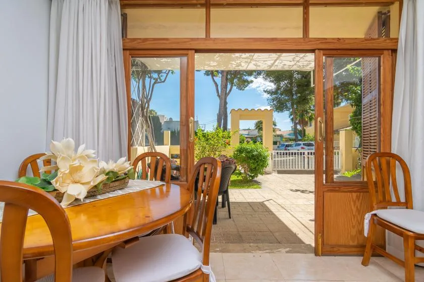 A wooden dining table and chairs sit beside open doors overlooking a sunny garden.