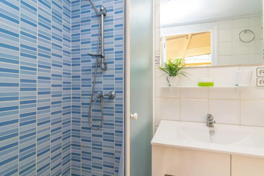 A bathroom with a blue-tiled shower and a sink beneath a mirror.