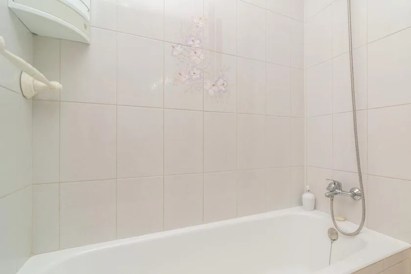 A tiled bathroom with a bathtub and wall-mounted shower fixtures.