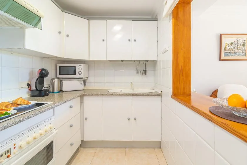 A bright kitchen with white cabinets, a countertop, and a pass-through window.