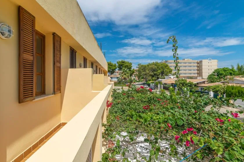 A balcony overlooks flowering greenery and nearby buildings under a blue sky.