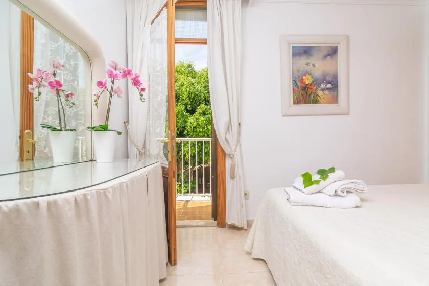 A bright bedroom with a bed beside an open balcony door and flowering orchids.