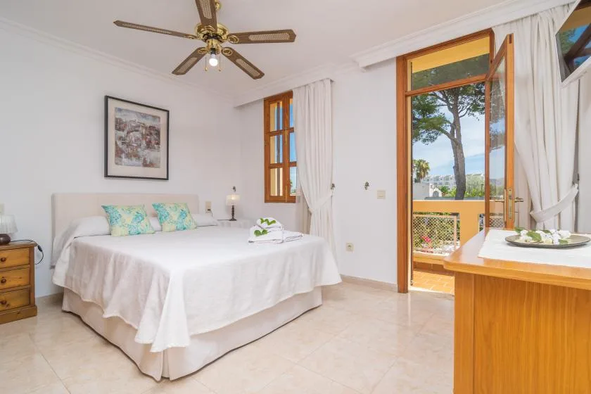 A bright bedroom with a bed, open balcony doors, and a view of trees.