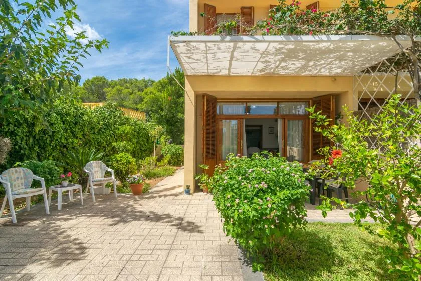 A garden patio beside a house, with outdoor seating and flowering plants.