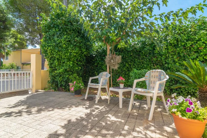 An outdoor patio with seating, potted flowers, and leafy greenery.