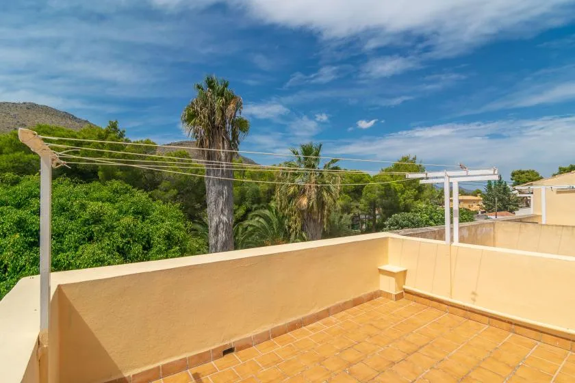 A sunlit rooftop terrace with tiled flooring and views of trees and hills.