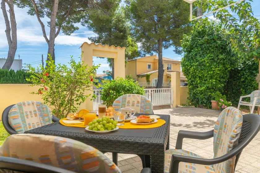 An outdoor dining area with a set table and patio seating beneath leafy trees.