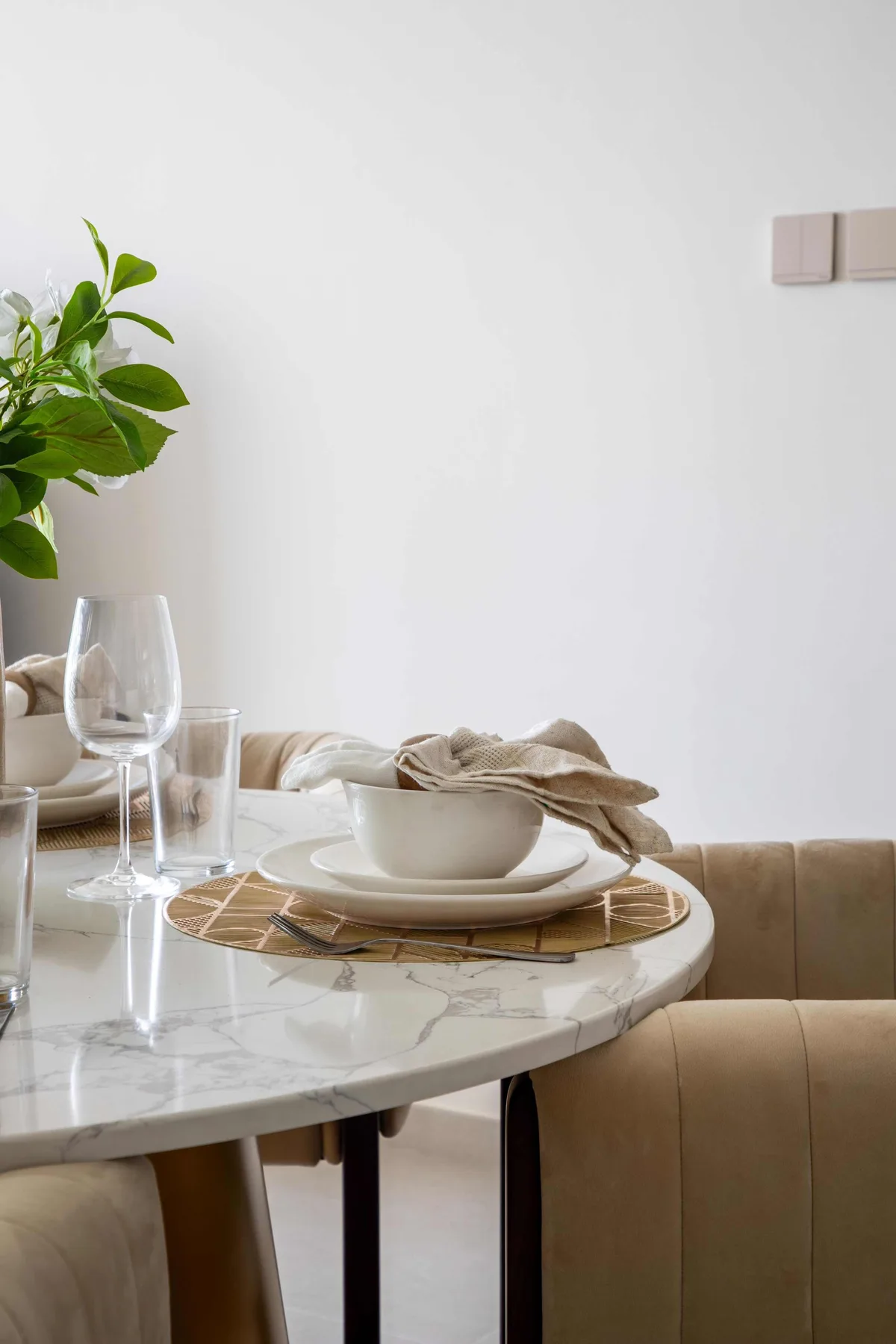 Una mesa de comedor está puesta con platos, copas y una planta frondosa.