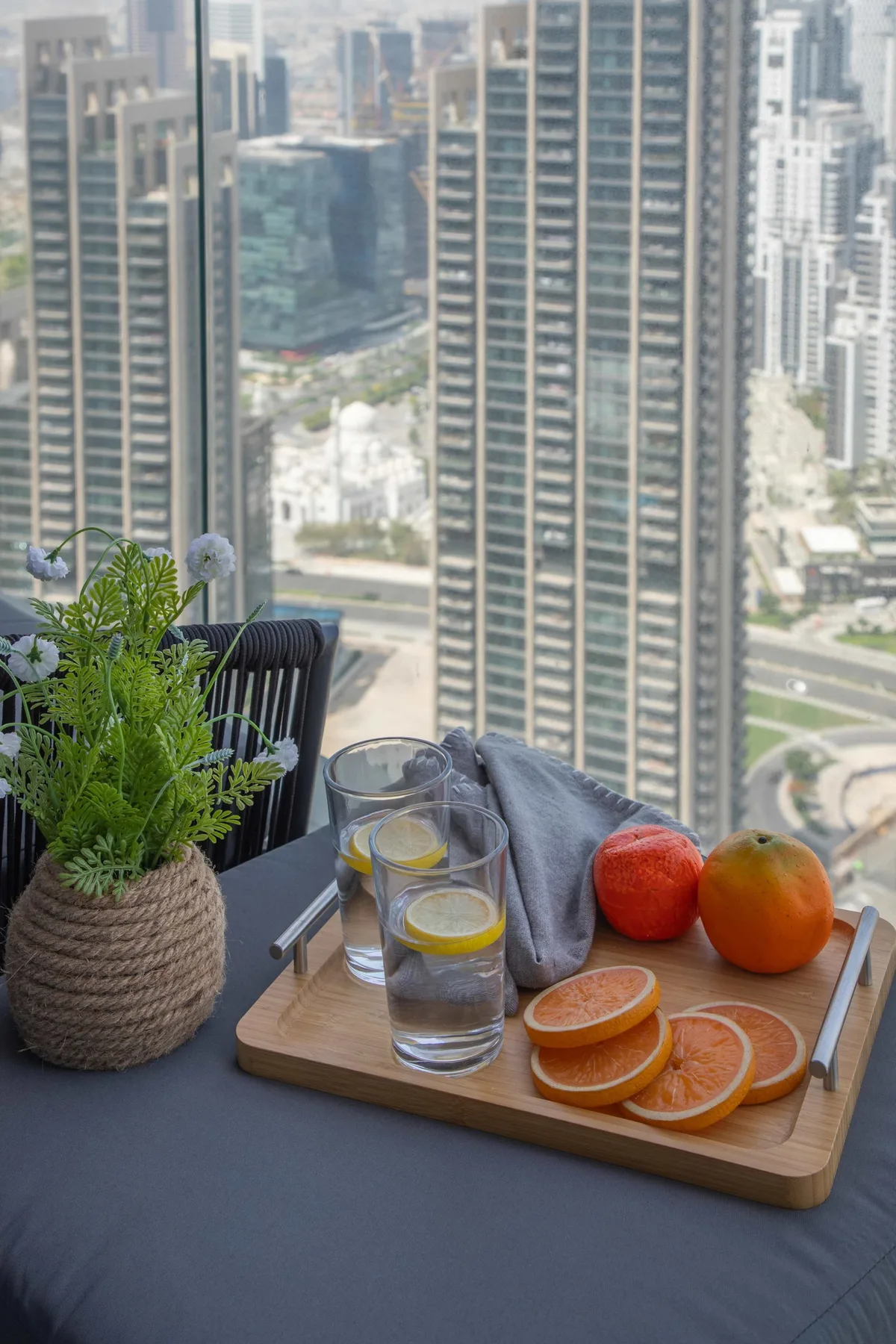 Una mesa junto a una ventana tiene cítricos, vasos de agua y una planta en maceta.