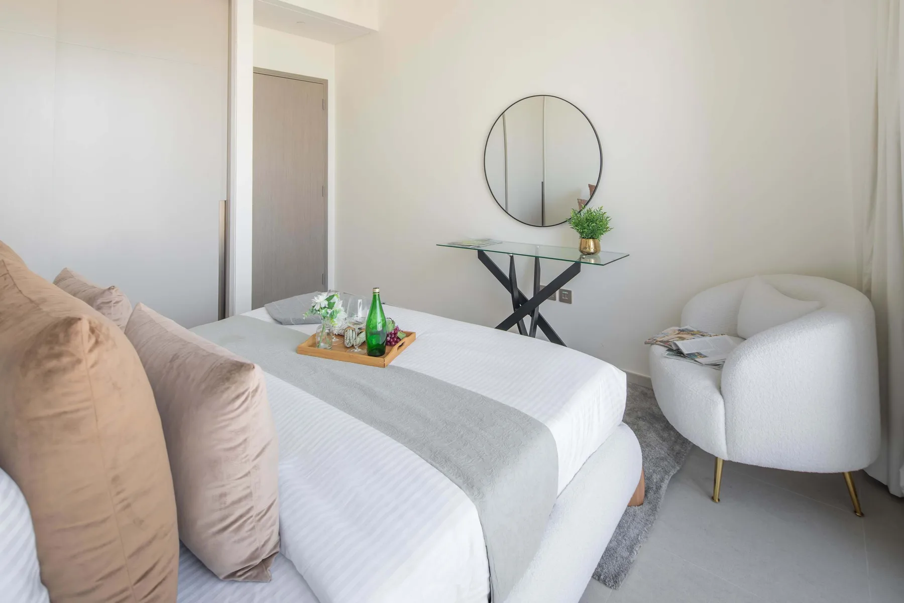 Un dormitorio con una cama, un espejo redondo en la pared y una pequeña mesa de vidrio.