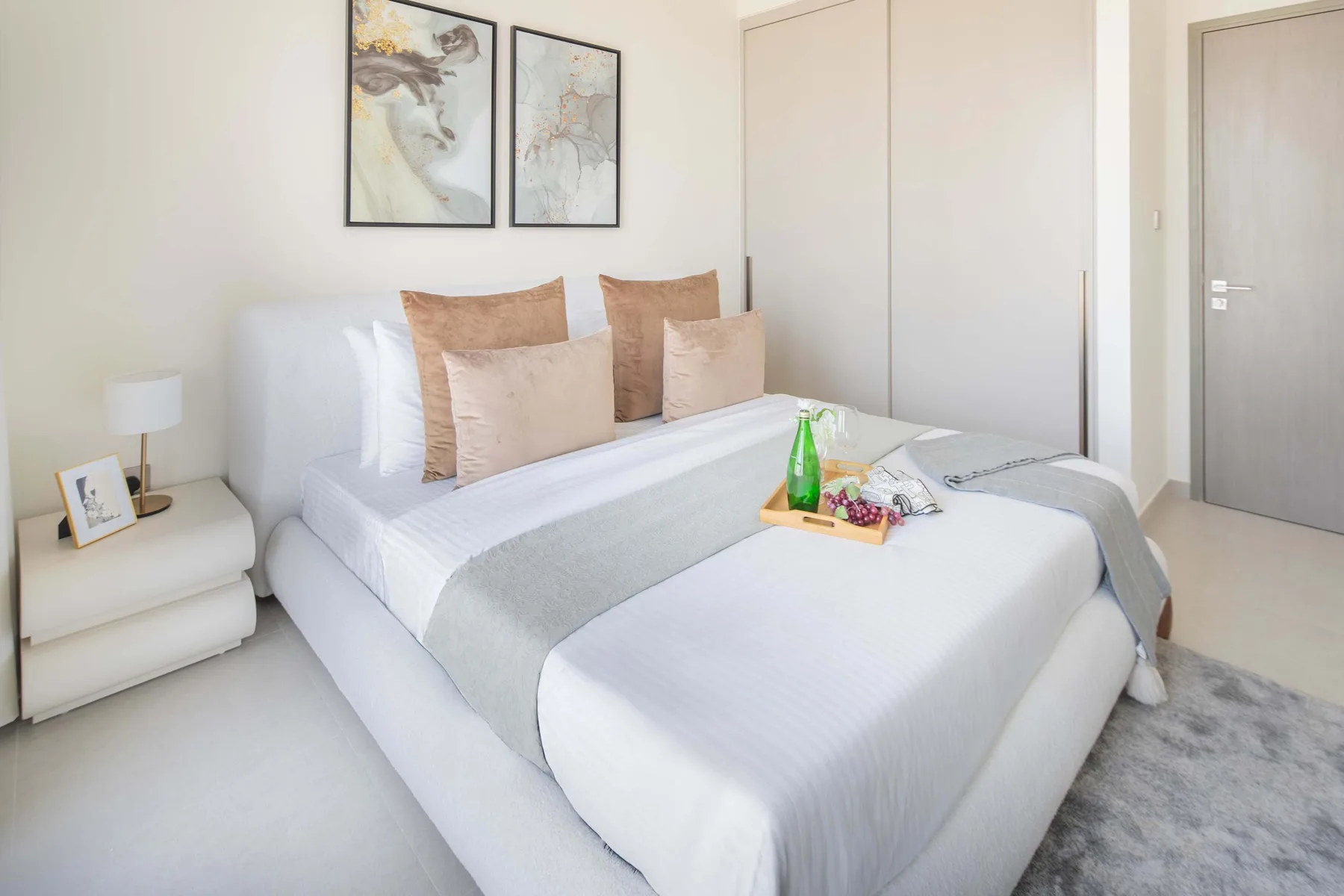 Un dormitorio luminoso con una cama bien arreglada y cuadros enmarcados encima.