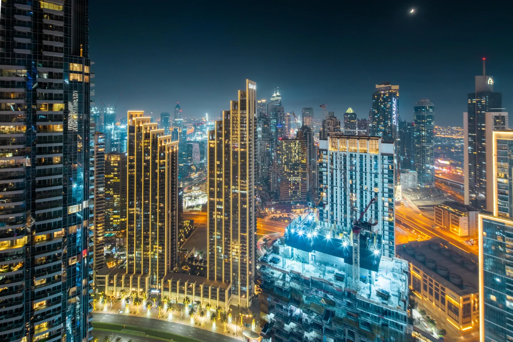 Un horizonte urbano nocturno con edificios altos iluminados y vías concurridas.
