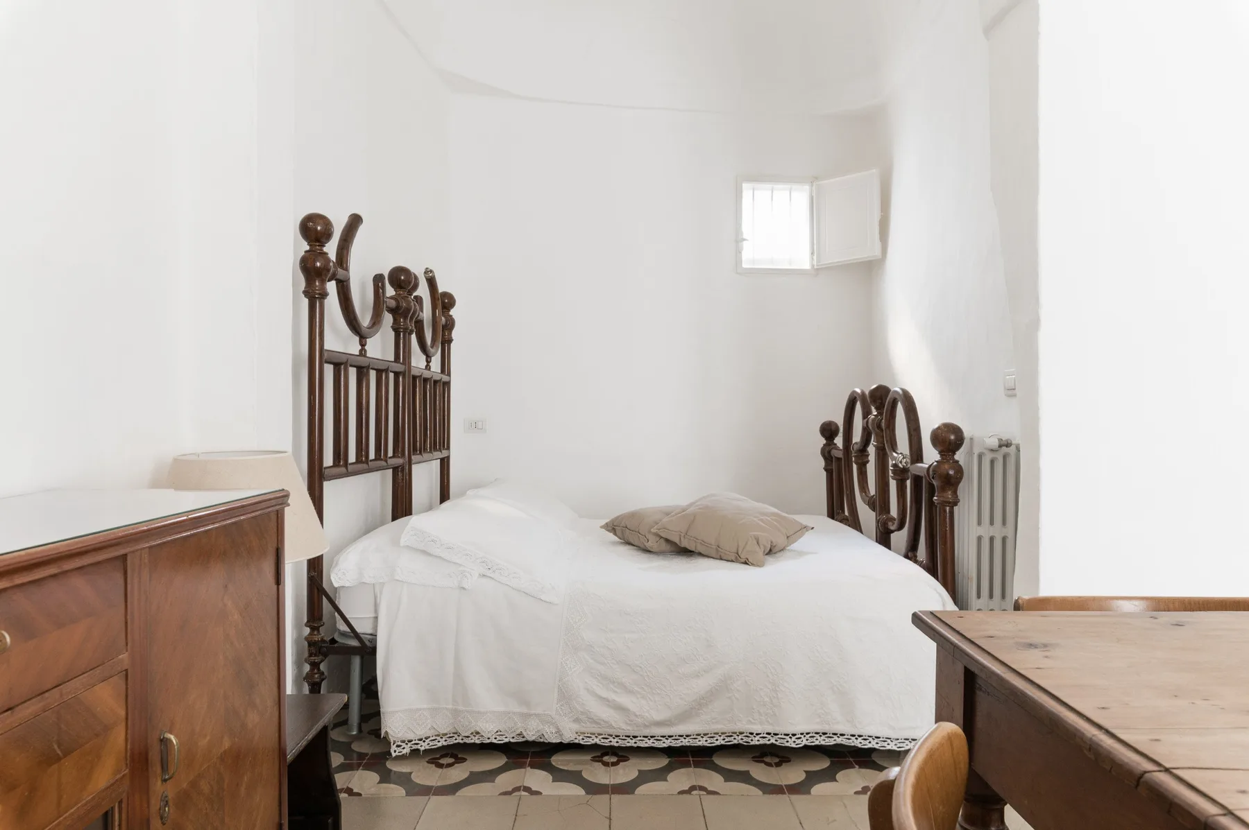 A white bedroom with a bed, dark wooden headboards, and wooden furniture.