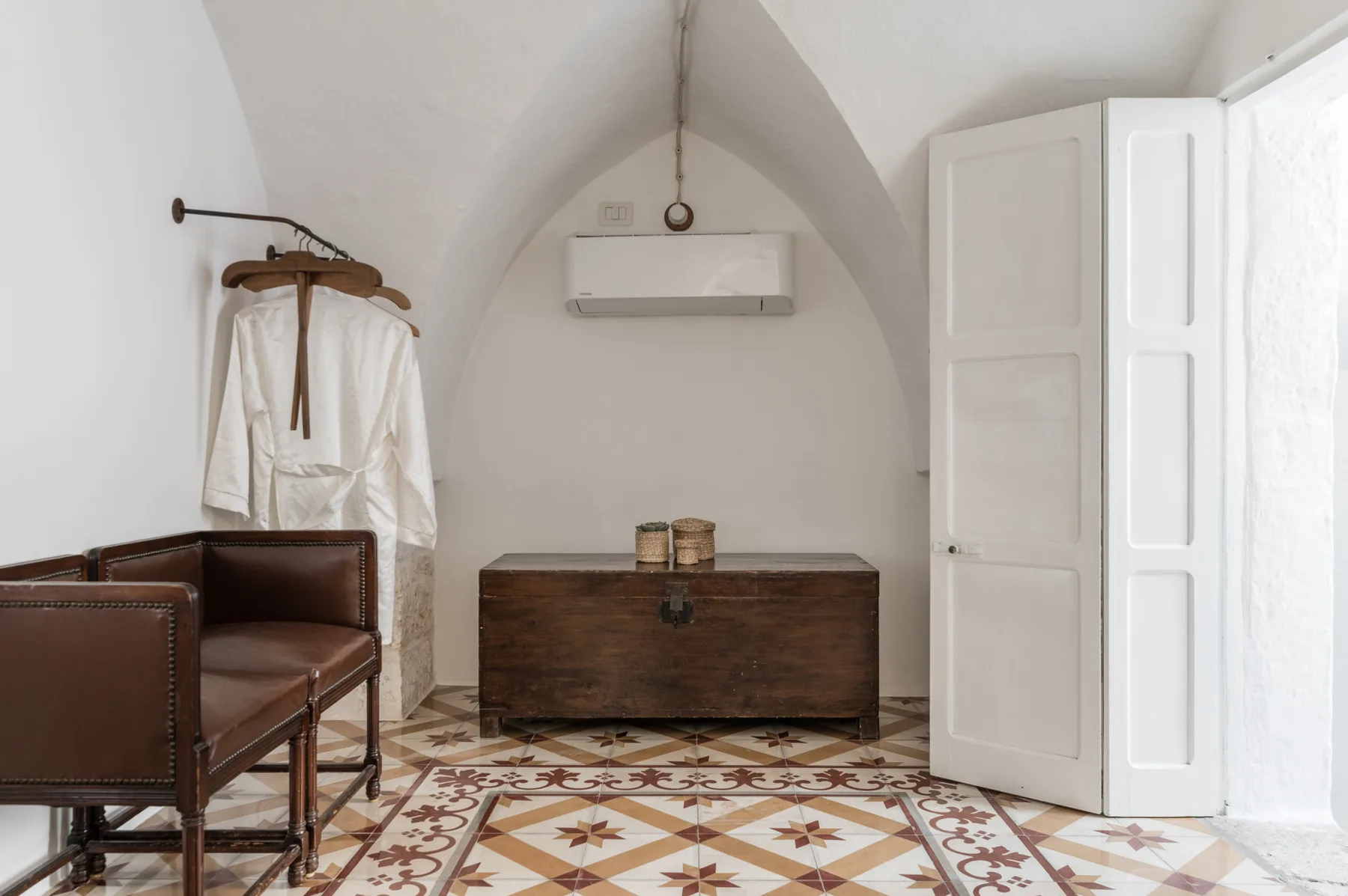 A vaulted room with a dark wooden chest and brown seating beside a tiled floor.