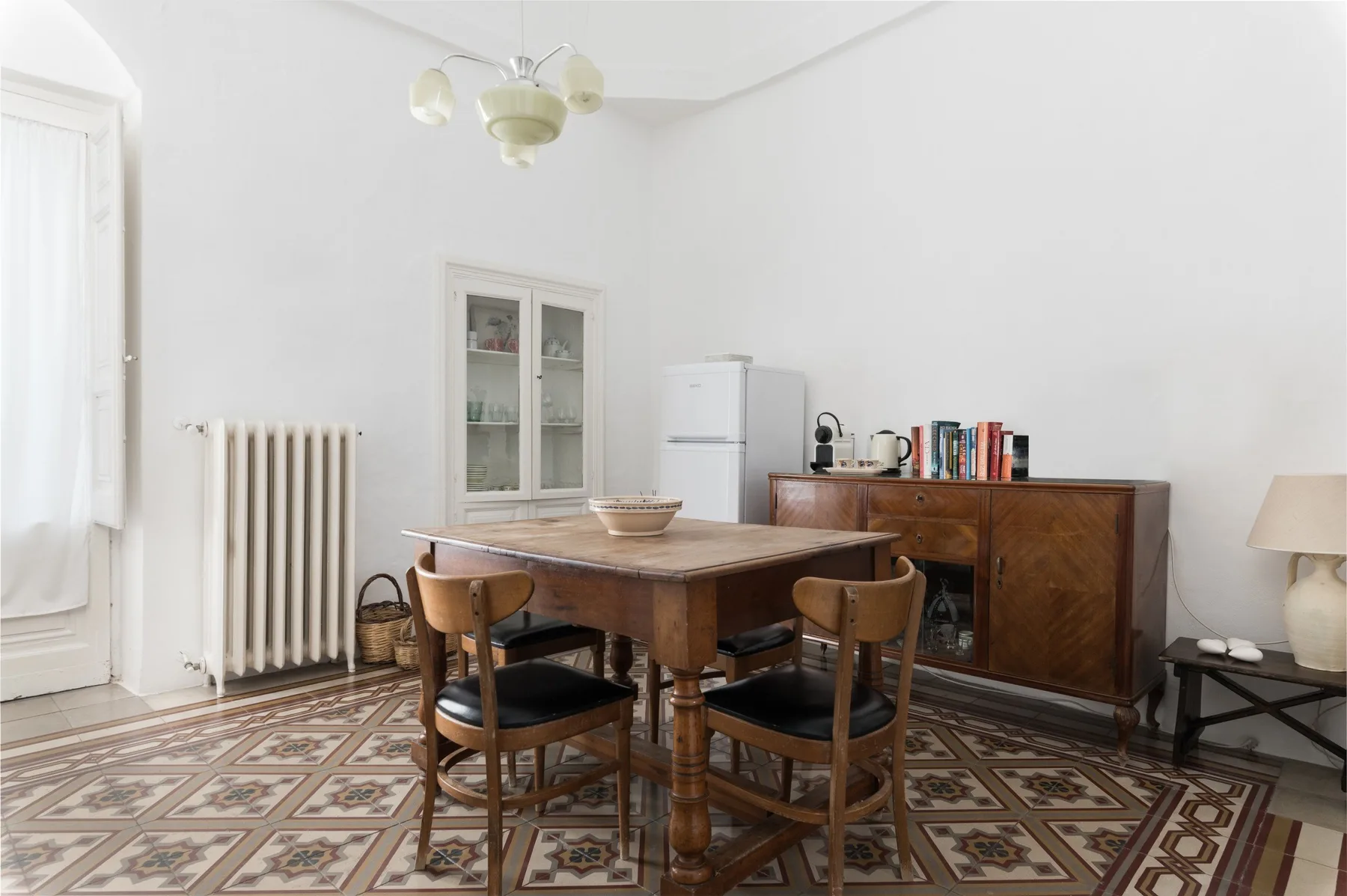 A dining area with a wooden table and chairs beside a cabinet and refrigerator.