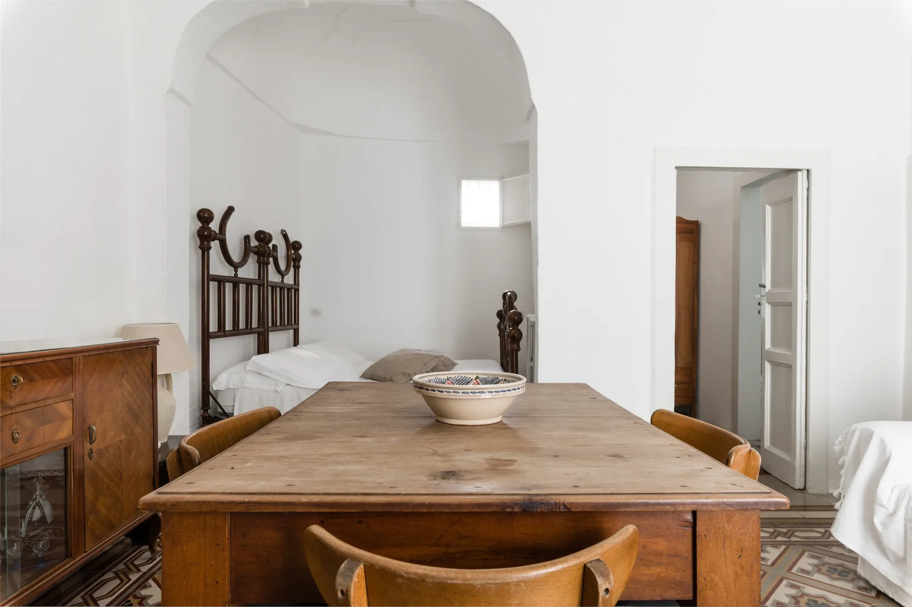 A bedroom with a wooden table and a bed beneath an arched alcove.