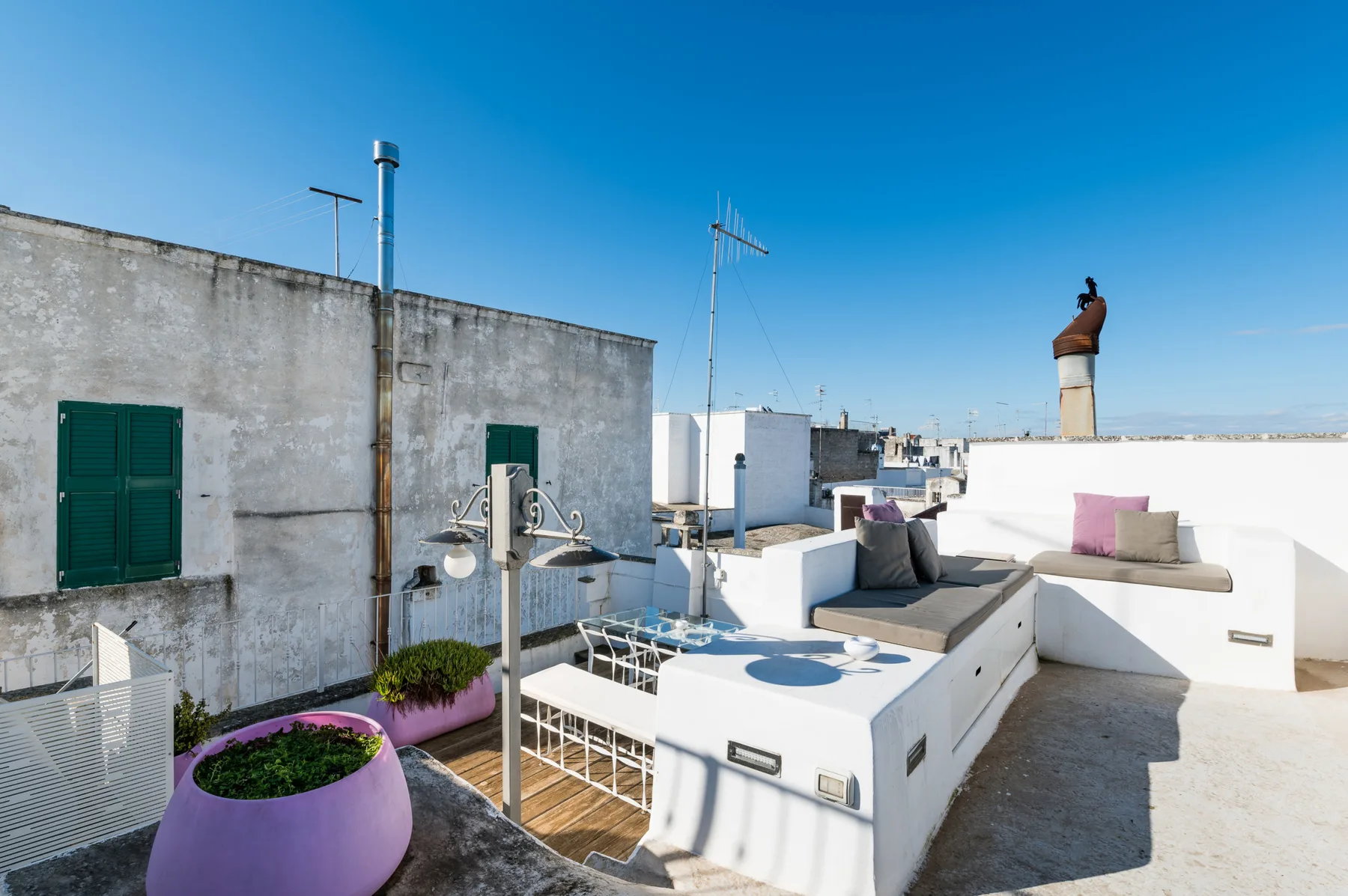A sunny rooftop terrace with built-in seating and a small planted area.