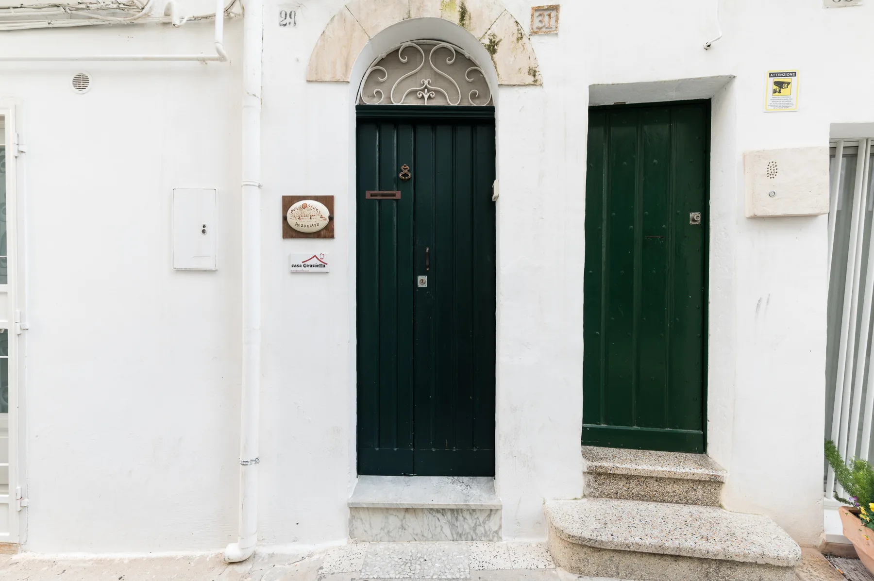 A white building facade with two dark green doorways and stone steps.