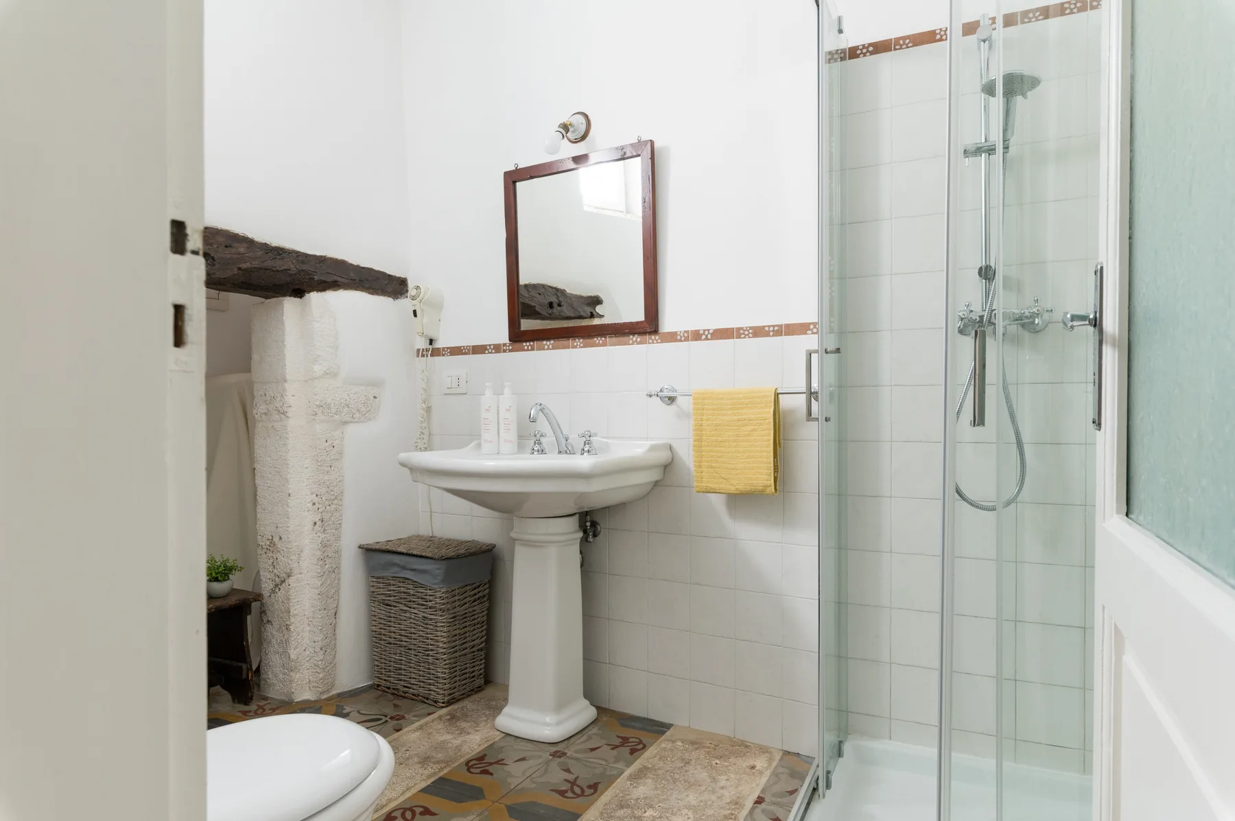 A bright bathroom with a pedestal sink, mirror, and glass shower.