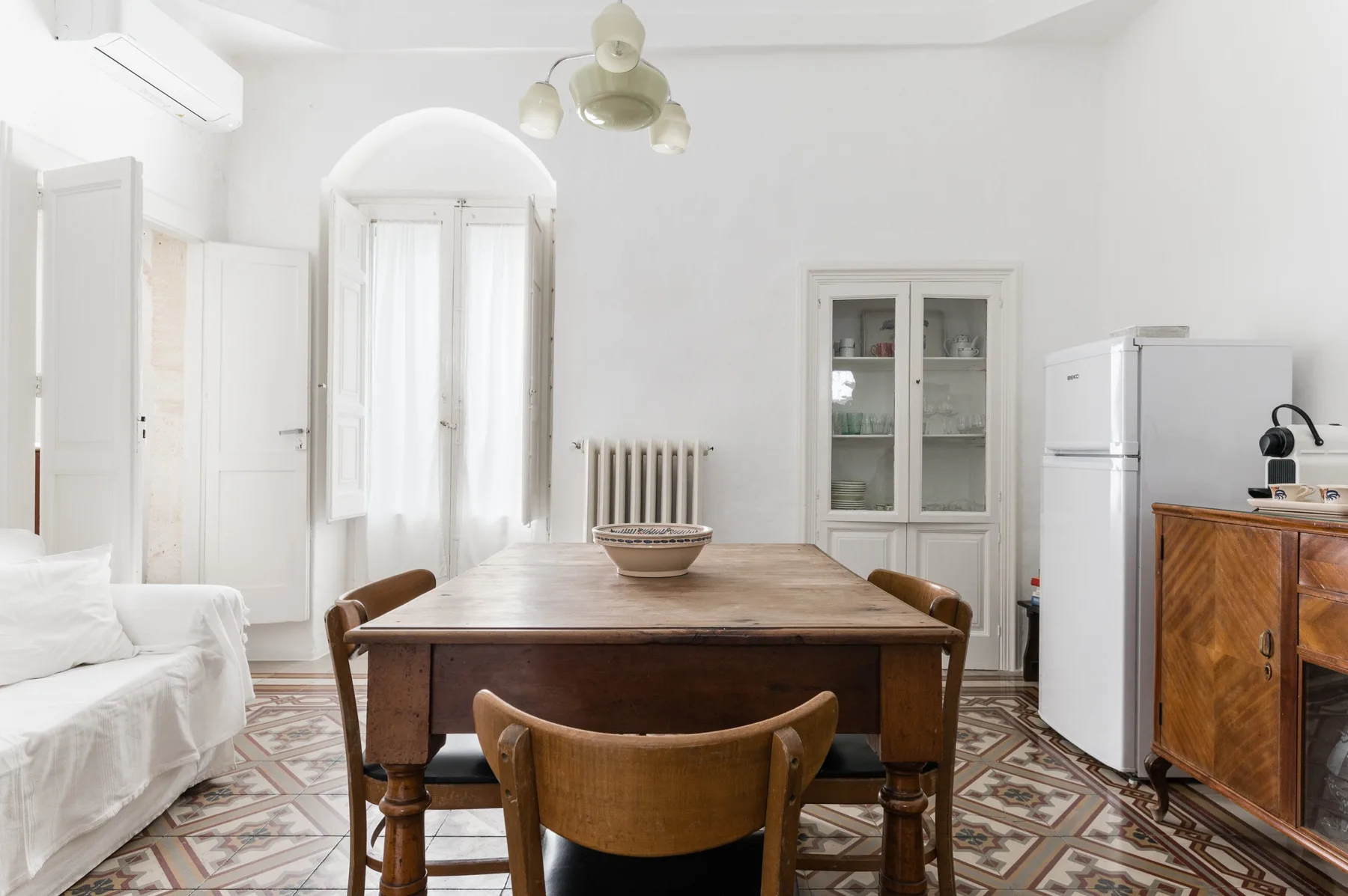 A bright dining area with a wooden table, seating, and a glass-front cabinet.