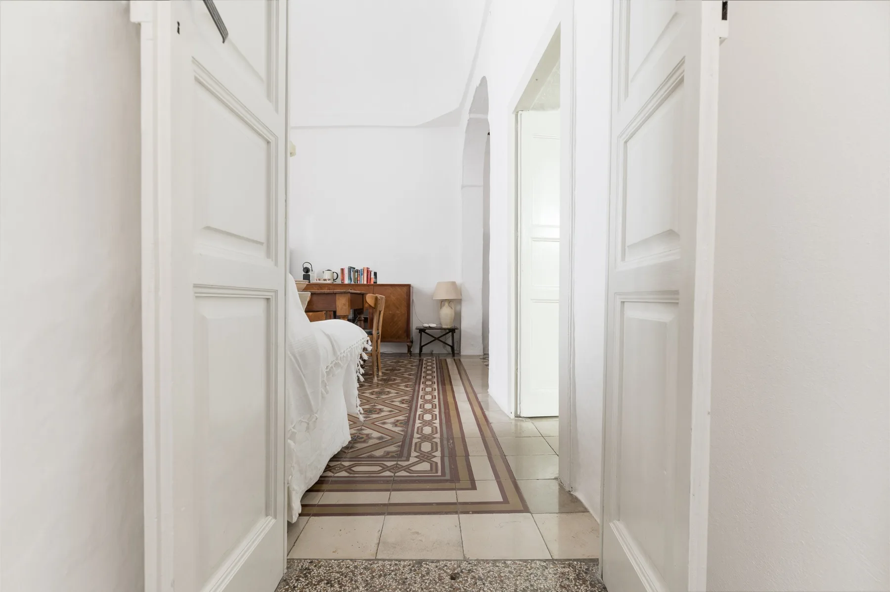 A bright bedroom is visible through an open doorway, with a patterned rug and wooden desk.