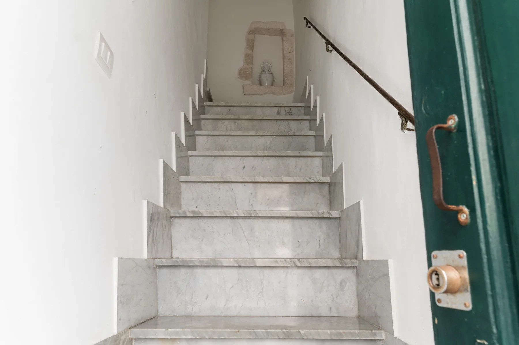 A marble staircase rises between white walls, with a dark handrail along one side.