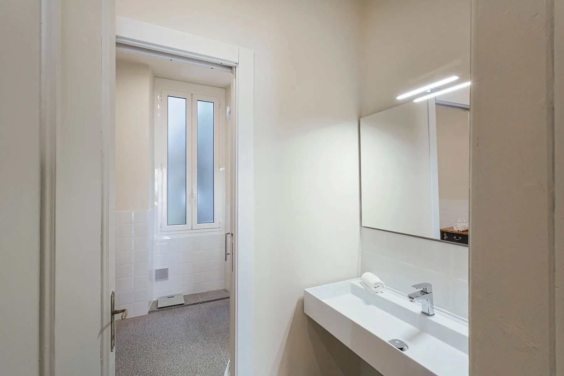 A bathroom vanity with a sink and mirror sits beside a doorway.