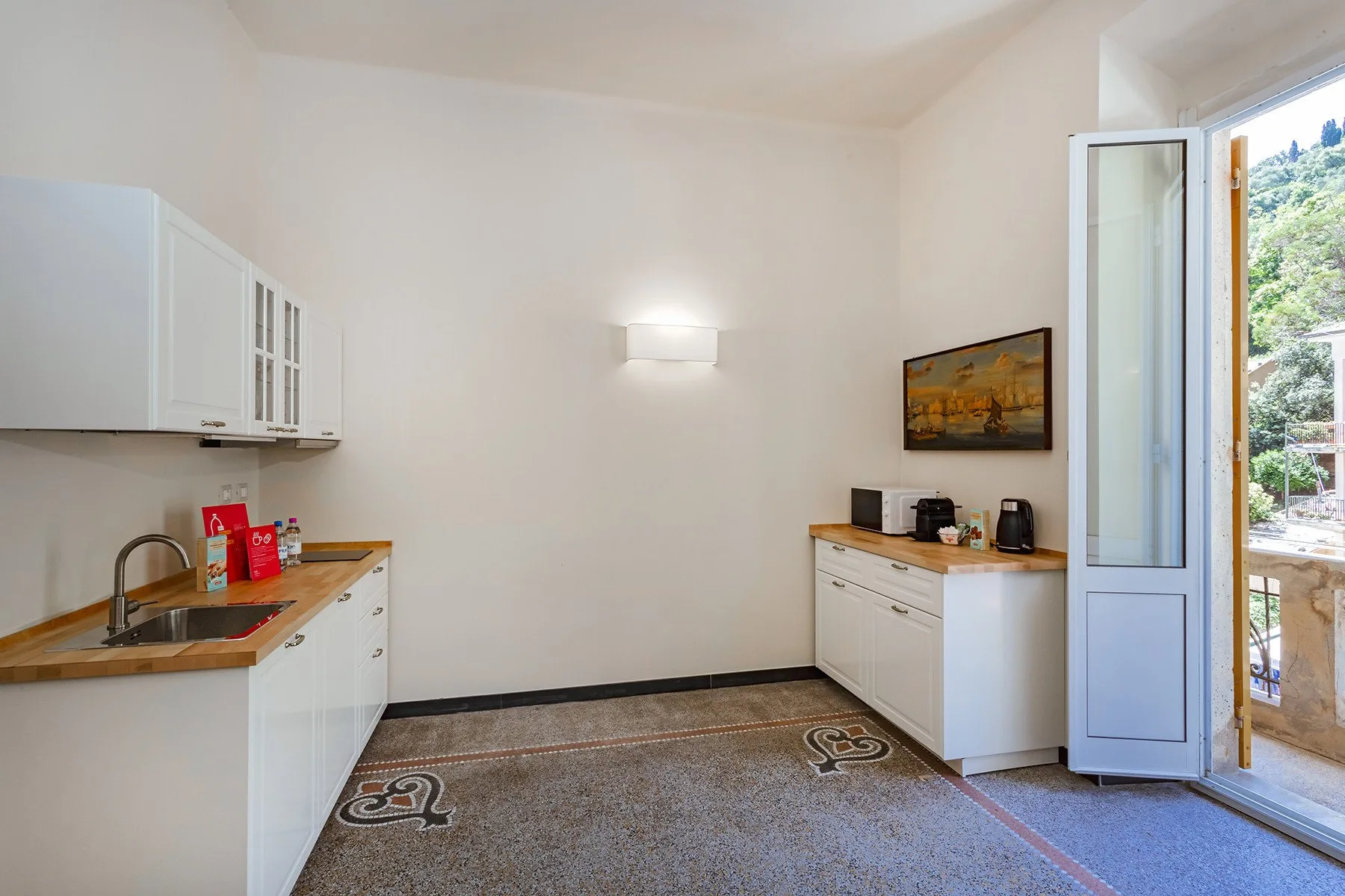 Una cocina luminosa con gabinetes blancos, encimeras y una puerta abierta al balcón.